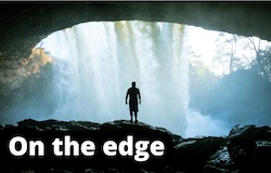 Photo of a man standing at the edge of cave under a water fall
