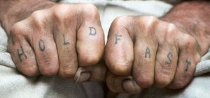 An image of two hands tattooed with the words Hold Fast as a reminder to stick with it when investing is boring